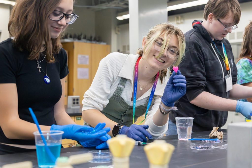 Astrin Krane, a Glastonbury High School student and second-year attendee of the Queer Science Conference, smilesat the camera and holds a pink heart-shaped alginate she made during a science demonstration and presentation about hydrogel crosslinking and application in the Chemistry Building during the conference on June 4, 2023. (Sydney Herdle/UConn Photo)
