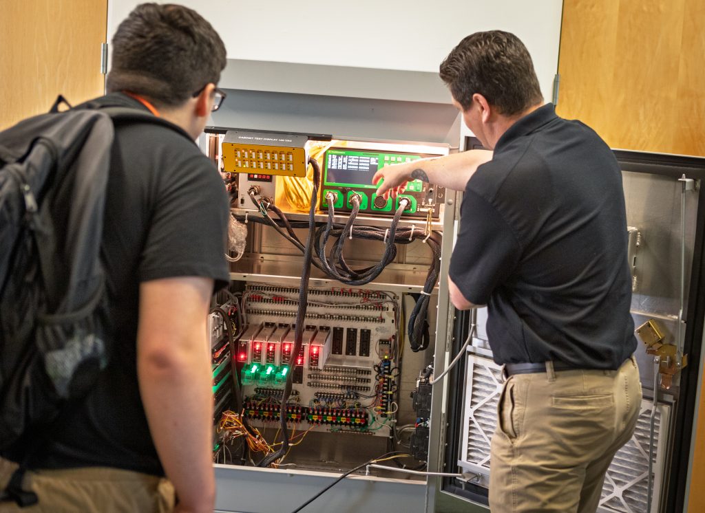 An engineer explaining the insides of a device to a student on Explore Engineering Day.