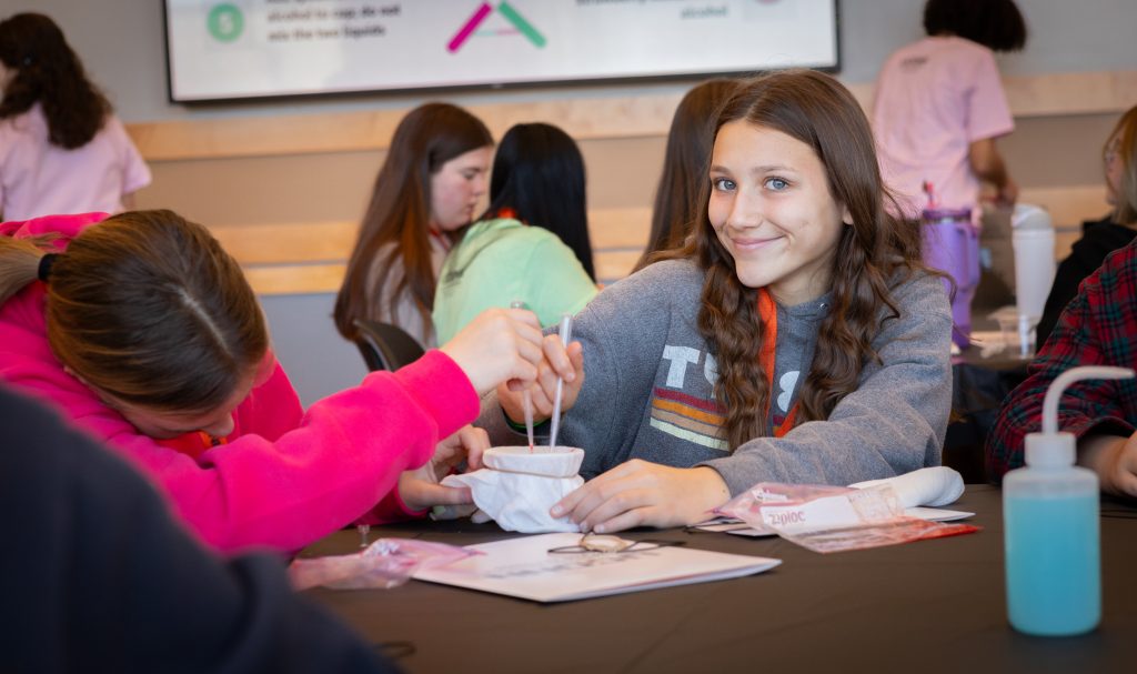 A photo taken at the Multiply Your Options event in the Student Union Ballroom of two 8th grade girls using plastic pipettes to do a scientific actvity.