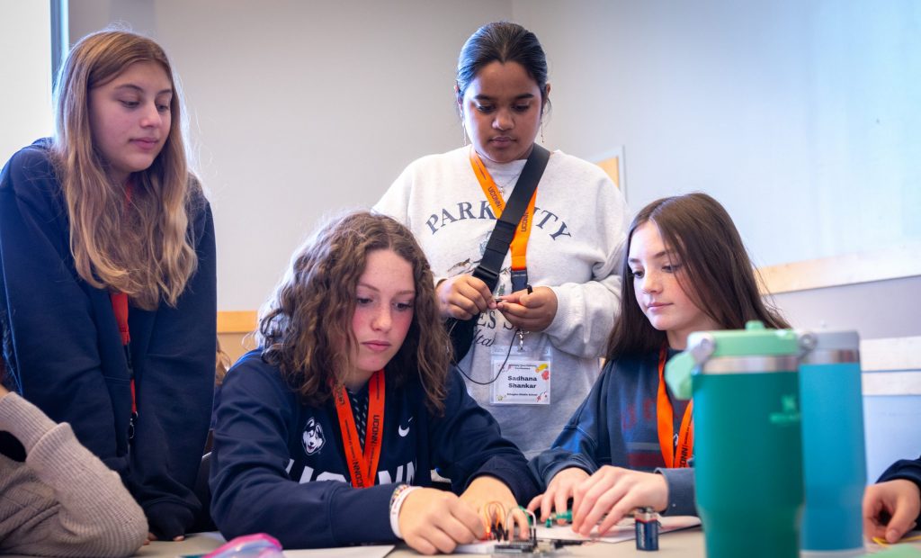 A photo taken at the Multiply Your Options event in the Student Union Ballroom of four 8th graders concentrating on a scientific actvity with electical components.