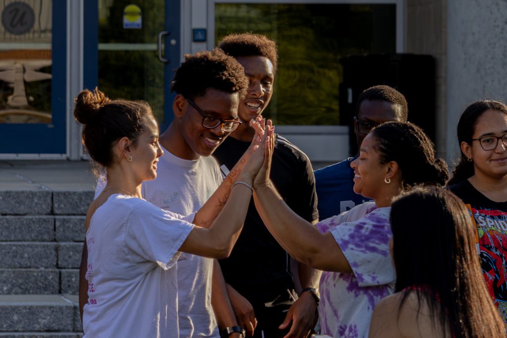 Students high-fiving eachother to celebrate during BRIDGE field day in front of the Student Union on the Storrs campus.