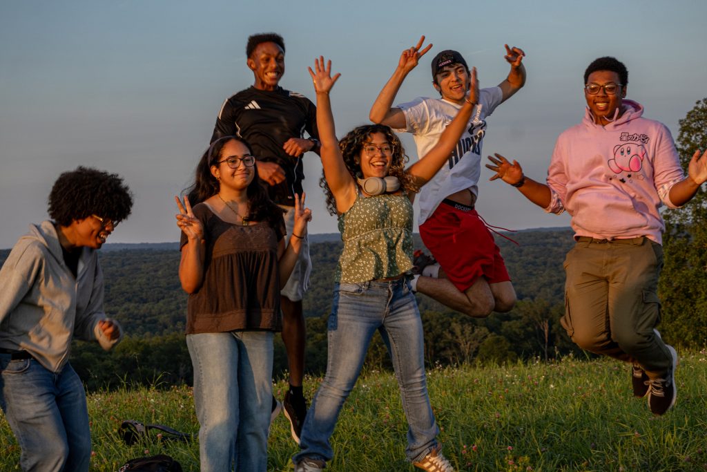 Smiling tudents jumping to take a photo at sunset on Horsebarn Hill.
