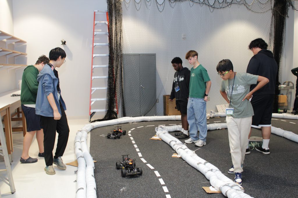 A group of students watching small autonomous vehicles on a model road.