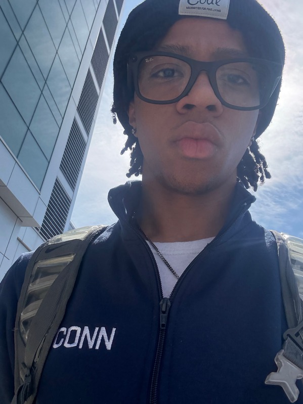 A selfie of Aiden walking whil wearing a UConn branded zip-up jacket and dark colored glasses.