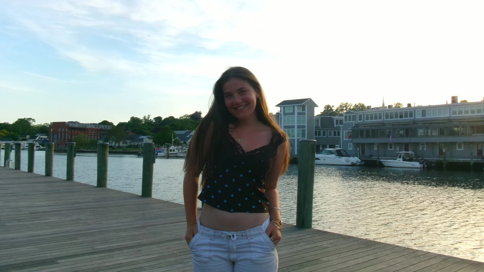 A photo of Ava taken on a wooden dock near a body of water, with buildings and small boats in the background.