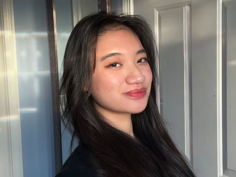 A photo of Briana wearing dark clothes, standing in front of a white door and blue wall.
