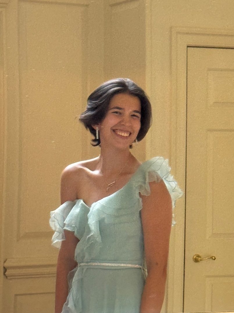 A photo of Izzy wearing a blue formal dress taken in the reflection of a gold, ornate mirror.