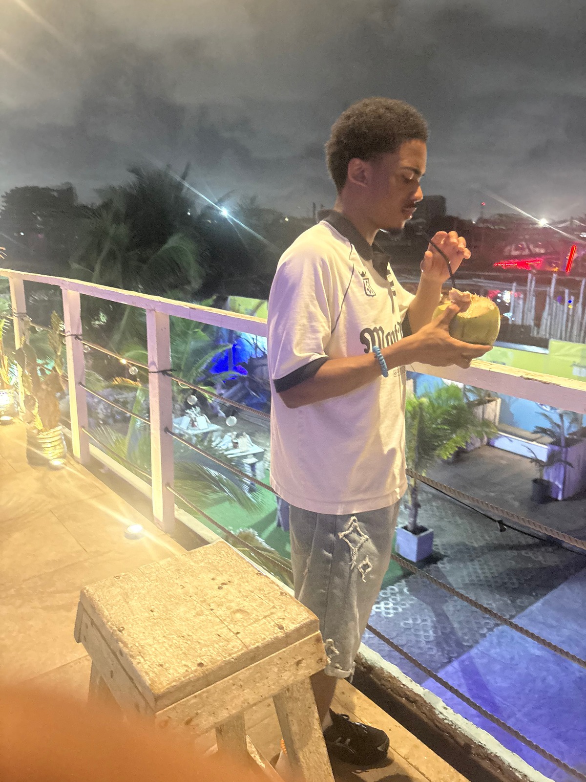 A photo of Mikey holding a beverage in a coconut on an outdoor patio at night.
